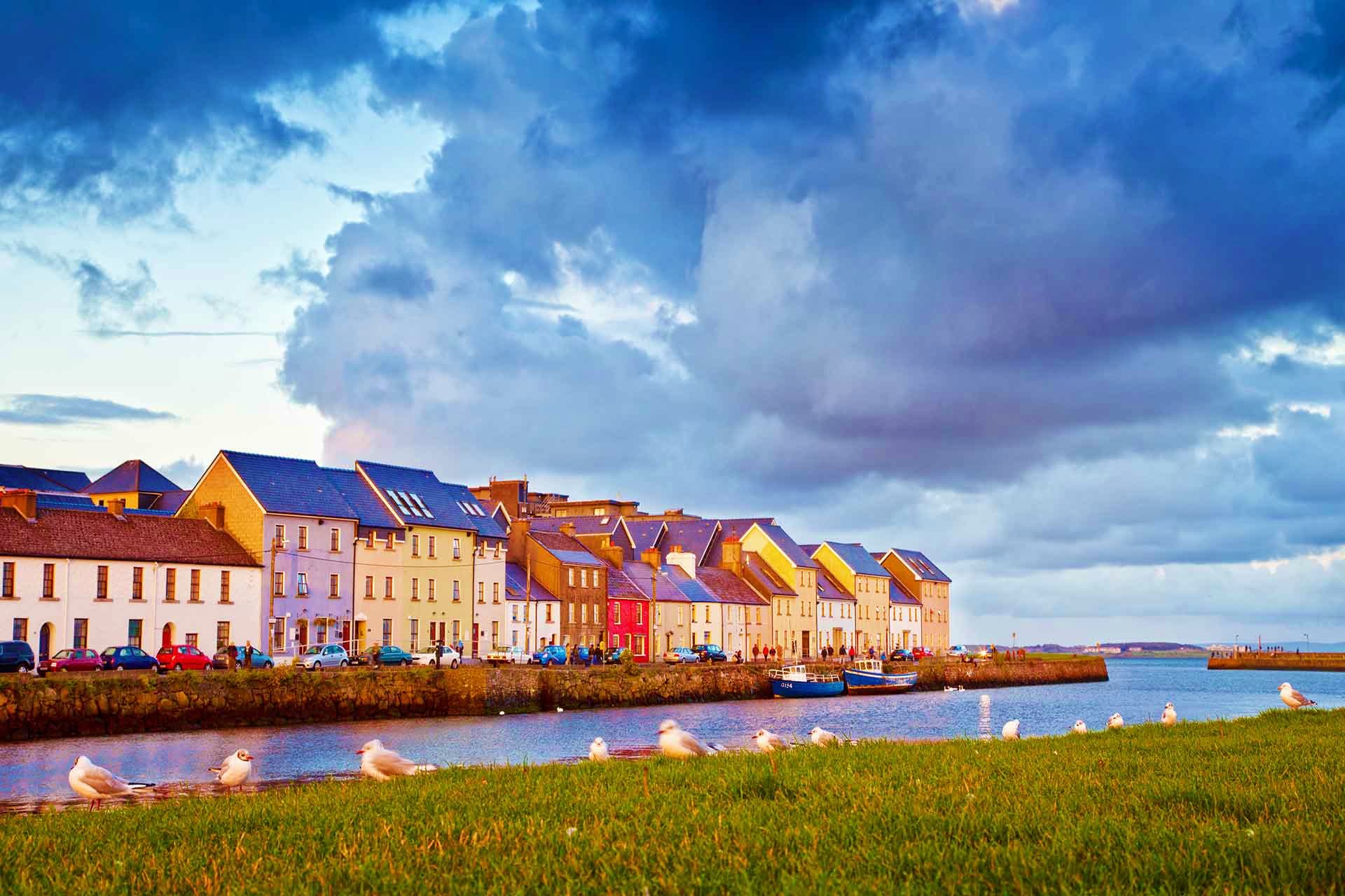 Colorful waterfront houses in Galway, Ireland with boats, seagulls, and dramatic sky